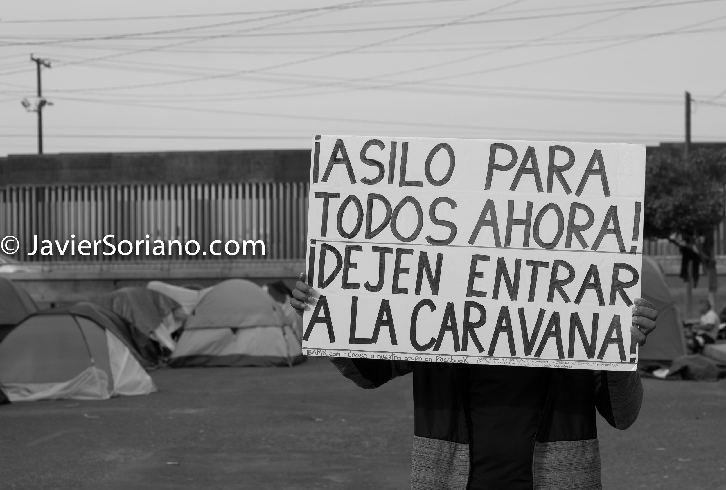 THIS PHOTO: Refugee from Centro America in Tijuana, Mexico. December/2018. Behind him is the Mexico - US border. The sign reads: "Asylum for everyone now! Let the caravan enter (the United States of America)". ESTA FOTO: Refugiado de Centro America en Tijuana, México. Diciembre/2018. Detrás de él está la frontera entre México y Estados Unidos. El cartel dice: "¡Asilo para todos ahora! Dejen entrar a la caravana (a los Estados Unidos de América)". Photo by Javier Soriano/JavierSoriano.com